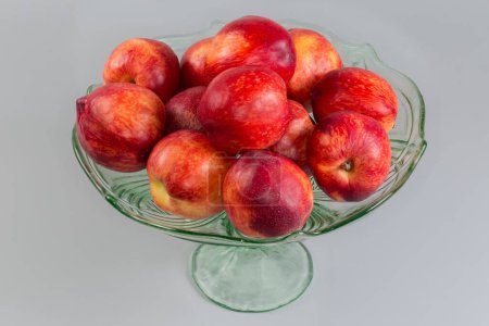 Fresh ripe nectarines on the vintage green glass fruit vase on a leg on a on a gray background
