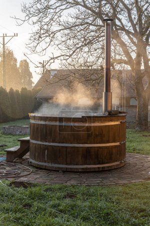 La sauna redonda de madera con agua caliente y vapor está afuera en otoño
