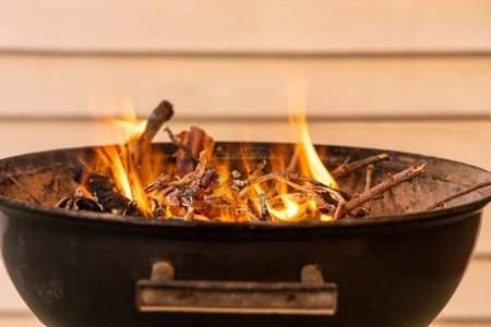 Téléchargez les photos : Le barbecue rond en métal noir avec feu pour un pique-nique est sur la terrasse - en image libre de droit