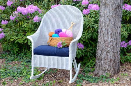 Téléchargez les photos : Fil coloré dans un panier sur un rocking chair en osier blanc dans un jardin de rhododendrons - en image libre de droit