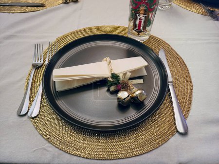 Photo for Gold Christmas bells on a black dinner plate setting with a gold metallic placemat - Royalty Free Image
