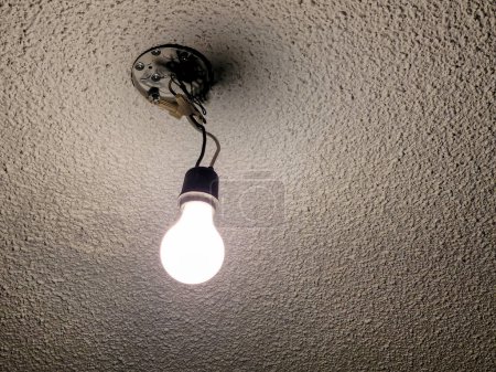 Glowing bare light bulb hanging from a light fixture on a popcorn ceiling