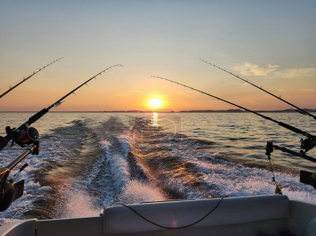 Foto de Postes de pesca en un barco de motor con estela de barco y el cielo del amanecer sobre el horizonte - Imagen libre de derechos