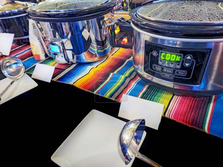 Reihe von Geschirrtöpfen auf bunt gestreiftem Tuch für einen Chili-Kochwettbewerb