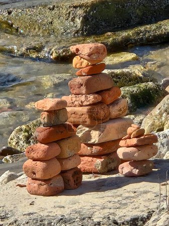 Cairn creado con viejos ladrillos de arcilla roja en rocas de playa a la luz del sol