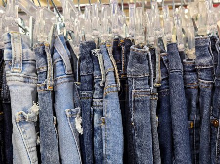 Close-up of distressed blue jeans clipped on clear plastic hangars in a boutique