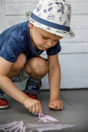 Photo for A boy draws with crayons on the asphalt . Painting. Summer games on the street. Childrens entertainment and leisure. Child puts a lot of effort and learns. - Royalty Free Image