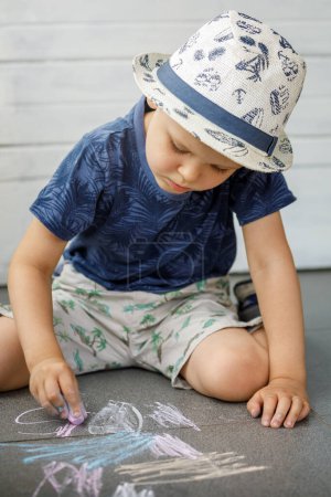 Photo for Little boy artist 3-4 years old, draws with crayons on pavement. The child is very focused. Children activities outdoors in summer - Royalty Free Image