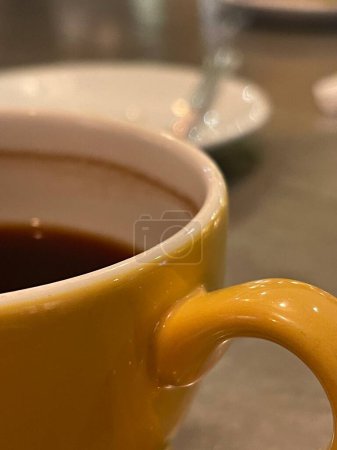 Foto de Cropped shot of black cpoffee served in a yellow cup - Imagen libre de derechos