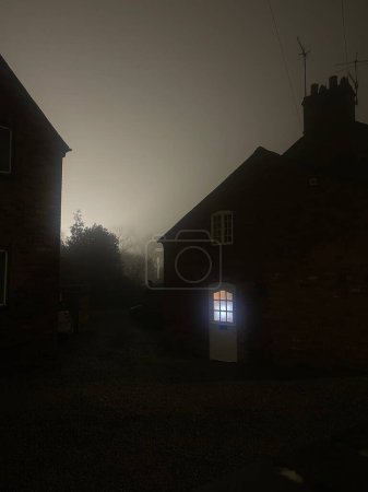 Téléchargez les photos : Window glowing in the door of a spooky house in the fog at night - en image libre de droit