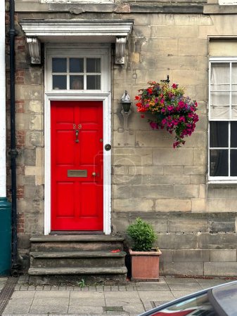 Photo for Vibrant red old fashioned door into an old house with beautiful potted flowers outside - Royalty Free Image