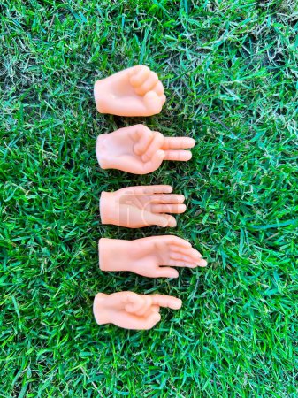 Téléchargez les photos : Jouets de marionnettes à doigts minuscules montrant différents gestes placés sur de l'herbe verte - en image libre de droit