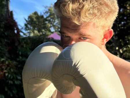 Téléchargez les photos : Gros plan d'un combattant masculin regardant férocement la caméra, portant des gants de boxe - en image libre de droit