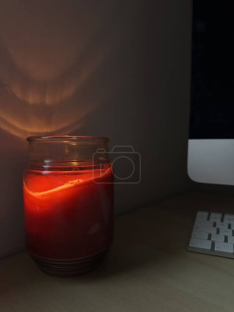 Téléchargez les photos : Bougie rouge brûlant sur un bureau avec l'ordinateur, lumière de feu de bougie réfléchie sur le mur - en image libre de droit