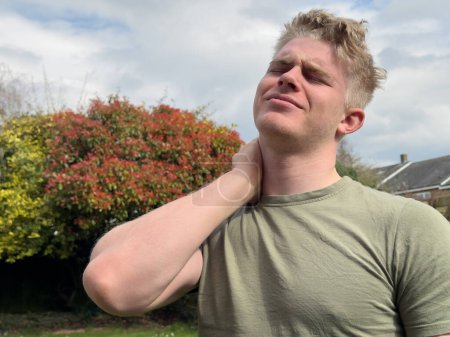 Photo for Young man massaging his aching neck standing outdoors - Royalty Free Image