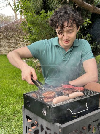 Vertical shot of a handsome young man grilling meat outdoors