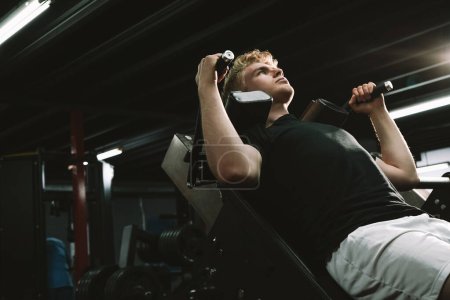 Low angle shot of a male athlete training at the gym, using hack squat machine