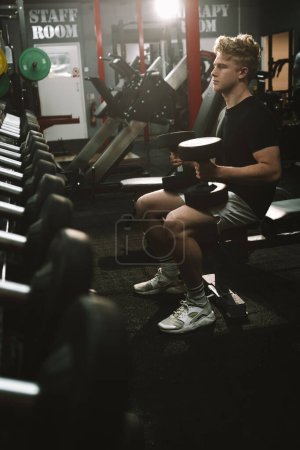Téléchargez les photos : Vertical shot of a handsome male athlete working out with dumbbells at the gym - en image libre de droit