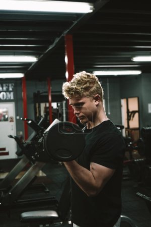 Photo for Vertical shot of a handsome muscular male athlete exercising with weights, doing biceps curls - Royalty Free Image
