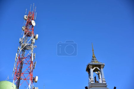 Photo for Telecommunication tower with antennas and building top against blue sky - Royalty Free Image