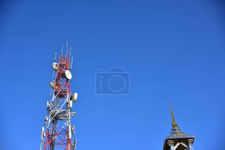 Telecommunication tower with antennas and building top against blue sky 