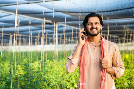 Téléchargez les photos : Happy smiling young farmer talking on mobile phone at greenhouse - concept of small business, modern farming and communication - en image libre de droit