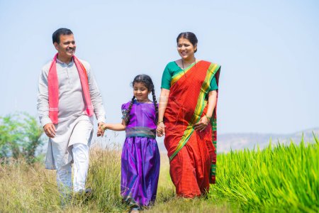 Téléchargez les photos : Heureux couple de village indien avec enfant marchant en parlant les uns des autres près de la rizière concept de mode de vie durable, liens familiaux et Inde rurale - en image libre de droit