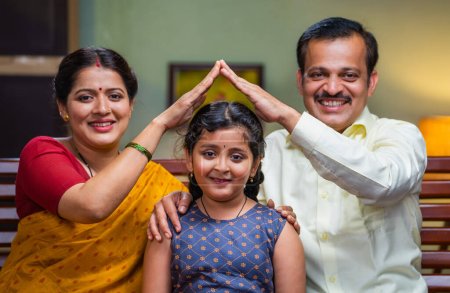 Téléchargez les photos : Couple indien heureux tenant la main comme geste de maison sur la fille en regardant la caméra concept de protection parentale, autonomisation et soutien ou développement de l'enfance. - en image libre de droit