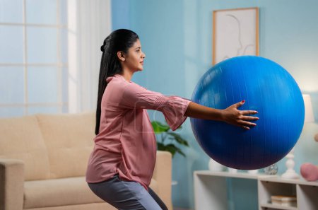Photo for Indian pregnant woman doing exercise by hoding fitness ball at home - conept of Maternity workout, active lifestyle and Endurance - Royalty Free Image