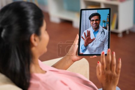 Téléchargez les photos : Plan de l'épaule d'une femme enceinte indienne consultant un médecin lors d'un appel vidéo à domicile - concept de télémédecine, soins de santé virtuels et consultation à distance - en image libre de droit