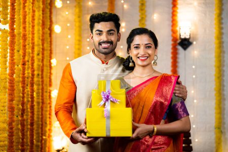 Glückliches junges indisches Paar mit Geschenkschachteln für das Diwali-Fest mit Kamera zu Hause - Konzept des Festverkaufs, Angebote und Überraschungsgeschenke zum Einkaufen