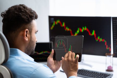 Shoulder Rack Fokus Shot des indischen Börsenmaklers oder Traders, der Charts auf dem digitalen Tablet im Büro checkt - Konzept der technischen Analyse, Investitionsplanung und Marktforschung.