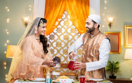 Foto de Feliz pareja india organizando fiesta de ramadán o preparación de alimentos hablando juntos en casa - concepto de relación, celebración del festival y Ramzan iftar. - Imagen libre de derechos