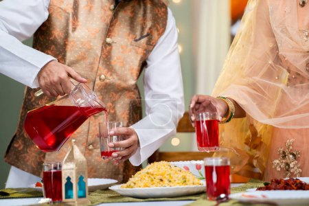 Gros plan du couple indien qui prépare une boisson à base d'eau de rose après le jeûne lors de la célébration du festival du ramadan à la maison concept de solidarité, de tradition et de Ramzan iftar.