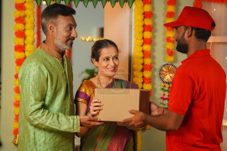 Senioren-Paare erhalten während des Diwali-Festes Pakete oder Pakete vom Zusteller an der Haustür - Konzept der Online-Bestellung, des schnellen Handels und des festlichen Geschenks oder Geschenks