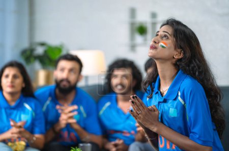 chica india preocupada con pintura facial y jersey rezando por ganar el partido mientras ve deportes de cricket - concepto de reunión de amigos, entretenimiento y emoción.