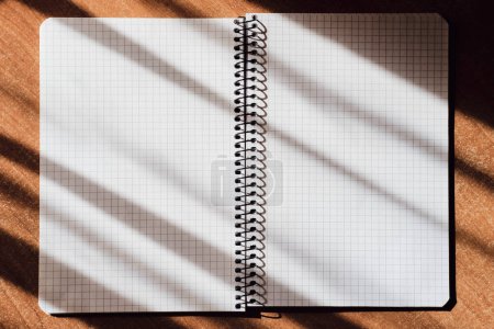 Photo for An open notebook in a cage lies on a table in sunny shadows - Royalty Free Image