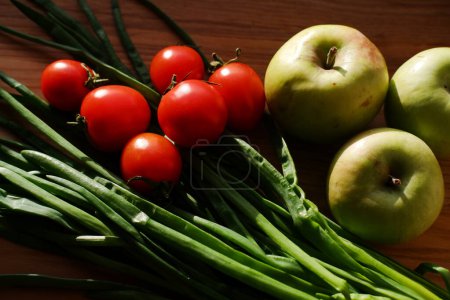 Téléchargez les photos : Légumes et fruits frais en gros plan sur une planche de bois. oignons verts, petites tomates cerises et pommes. préparation pour la cuisson - en image libre de droit
