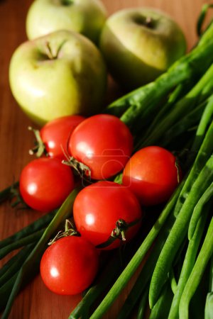 Téléchargez les photos : Légumes et fruits frais en gros plan sur une planche de bois. oignons verts, petites tomates cerises et pommes. préparation pour la cuisson - en image libre de droit