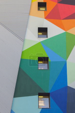 Fachada vertical pintada en colores formando triángulos con cuatro ventanas