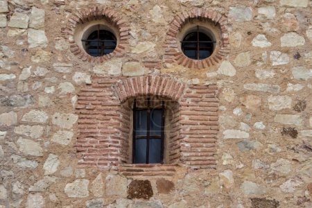 Foto de Pareidolia. Dos ventanas circulares y una ventana alargada, que se asemeja a una cara en un muro de piedra en la localidad de Pedraza, provincia de Segovia. España - Imagen libre de derechos