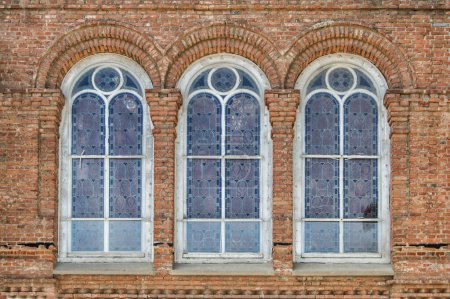 three identical windows with stained glass on a brick facade