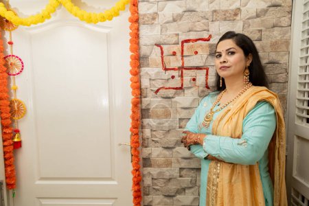 Glückliche junge Indianerin steht in ihrem neuen Haus mit Hakenkreuz-roter Farbe im Hintergrund. Griha Pravesh-Konzept