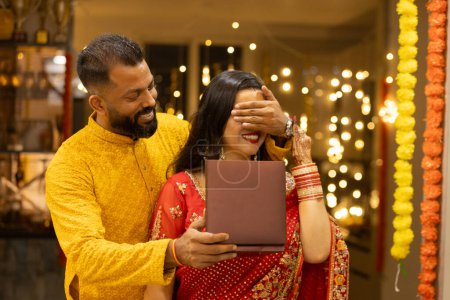 Junge indische Ehemann überrascht seine Frau, indem sie ihren kostbaren Schmuck Geschenk auf Diwali oder Hochzeitstag. Mann und Frau in traditioneller Tracht anlässlich des Festes.