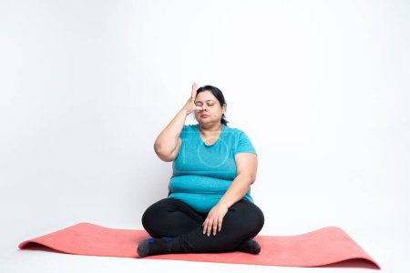 Overweight fat indian sitting on yoga mat doing yoga or Kapalbhati Pranayama. isolated over white background. Plus size female. copy space