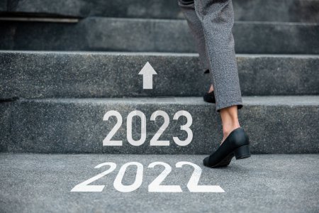Feliz año nuevo 2023. Al subir escaleras en la ciudad, las piernas de primer plano de la mujer de negocios se apresuran a caminar por las escaleras de 2022 a 2023, los pies de la mujer de negocios usan zapatos negros aumentan el éxito los próximos años