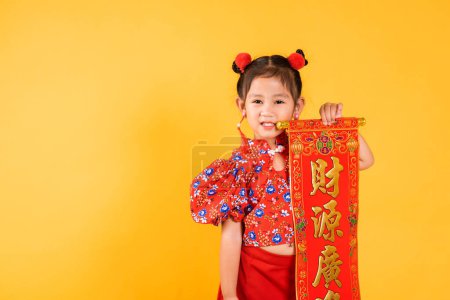 Photo for Chinese New Year. Happy Asian Chinese little child girl smile wearing red cheongsam qipao Spring festival couplets Character means fortune, blessing, studio shot isolated on yellow background - Royalty Free Image