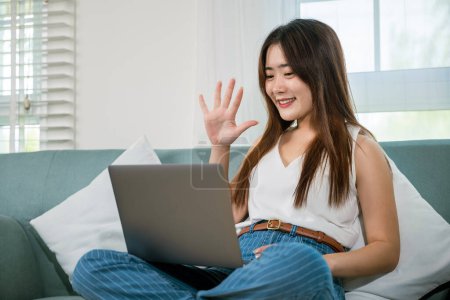 Happy woman browsing through the internet during free time on laptop computer, Female smiling sit on sofa using laptop in living room at home, girl shopping or chatting online in social media network Poster 624639282