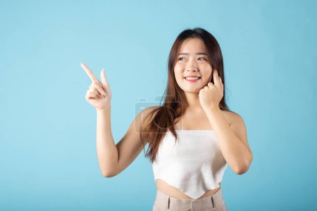 Photo for Beauty skin care. Asian beautiful young woman finger pointing to empty copy space studio shot isolated on blue background, Portrait female perfect skin point presenting for your product - Royalty Free Image