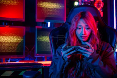 Téléchargez les photos : Gamer jouer application de jeu en ligne sur téléphone mobile porter casque de jeu, Asiatique femme en direct flux elle jouer à un jeu vidéo via smartphone à la maison néon lumières salon - en image libre de droit